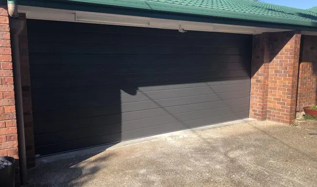Open carport enclosed with a dark automatic sectional garage door