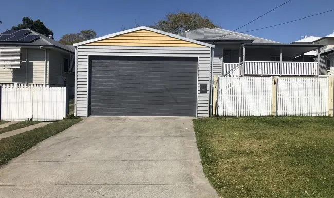 Grey sectional garage door on a detached garage with a yellow gable and white picket fence