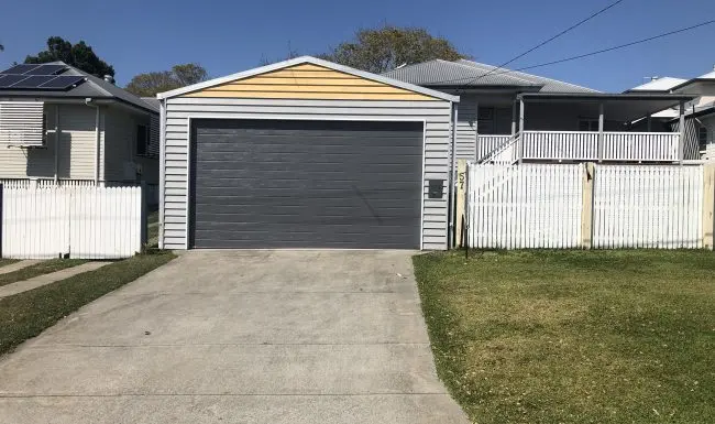 Grey sectional garage door on a detached garage with a yellow gable and white picket fence