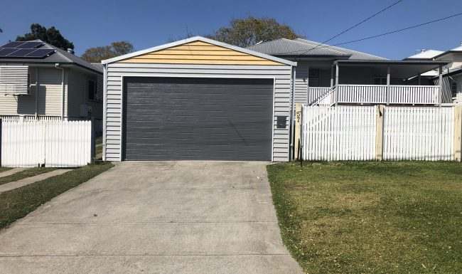 Grey sectional garage door on a detached garage with a yellow gable and white picket fence