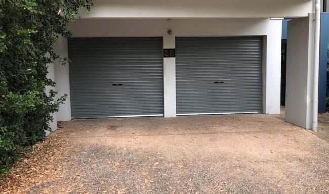 Two grey roller doors side by side beneath a rendered unit block carport
