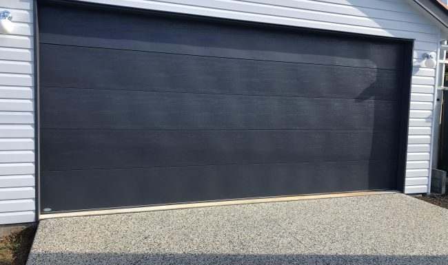 Wide charcoal flatline sectional garage door fitted to a white weatherboard garage