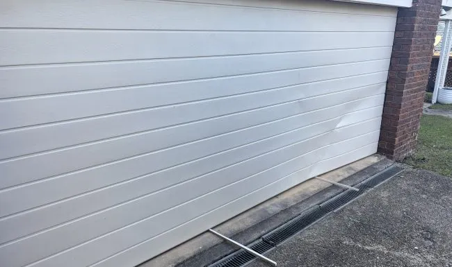 Cream sectional garage door seen along its closed edge beside a brick pier