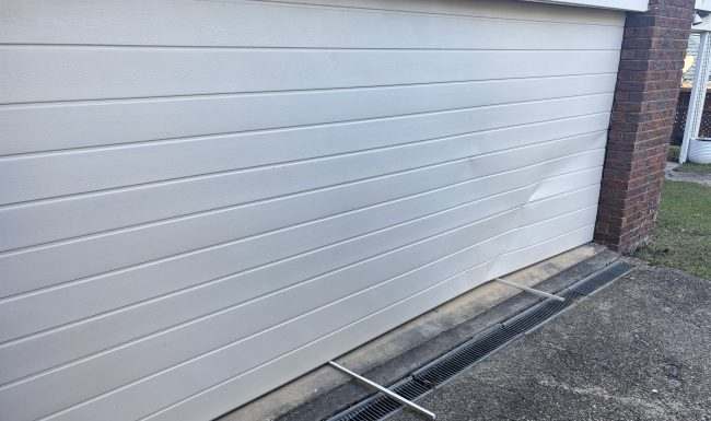 Cream sectional garage door seen along its closed edge beside a brick pier