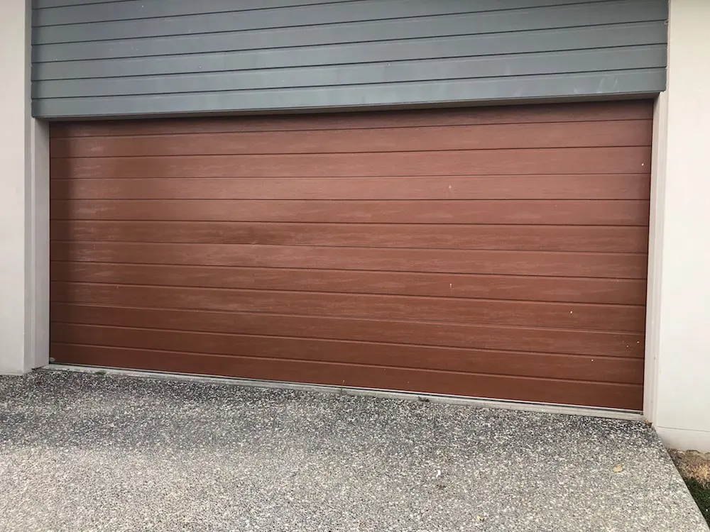 Woodgrain sectional garage door with damage across the lower panels