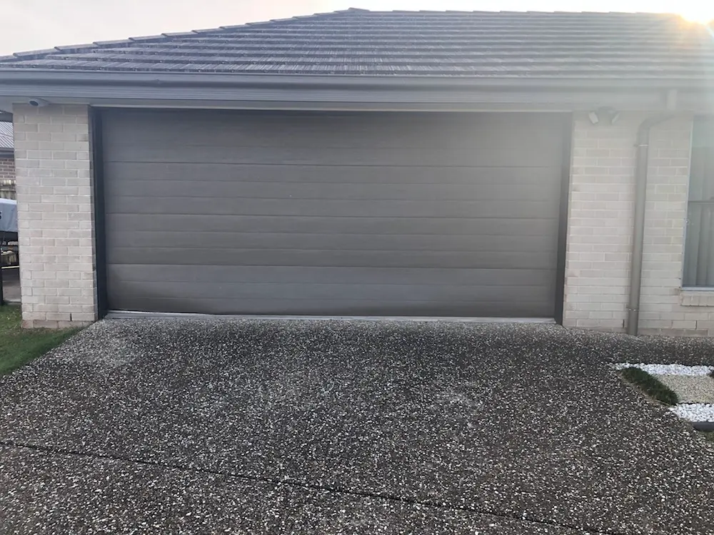 Dark charcoal sectional garage door on a brick home, before replacement