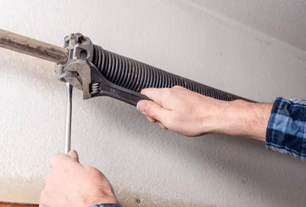 Torsion spring being wound with a winding tool on a garage door shaft