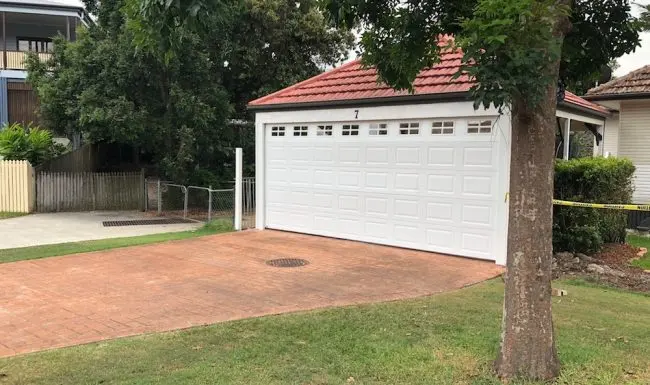 The same carport closed in with a white raised-panel garage door with top windows