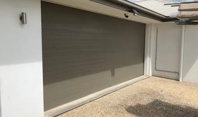 Grey-brown sectional garage door closed against a rendered wall beside an outdoor light